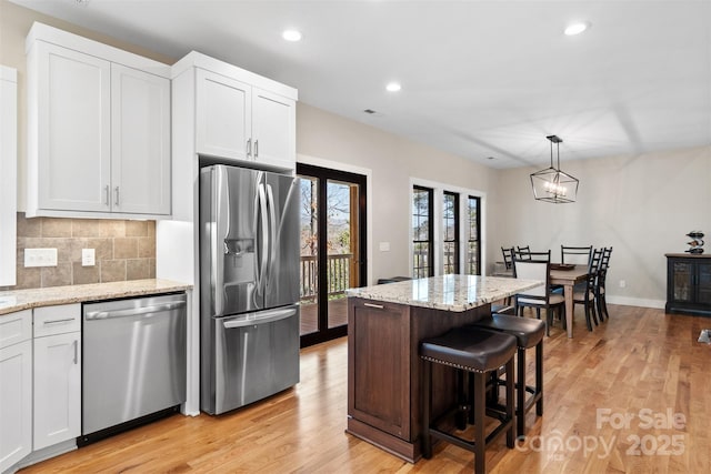 kitchen featuring appliances with stainless steel finishes, white cabinets, backsplash, and light wood finished floors