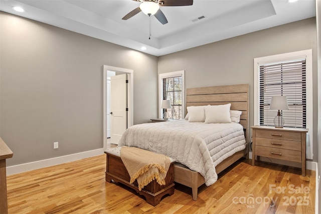 bedroom featuring light wood finished floors, baseboards, visible vents, and a tray ceiling