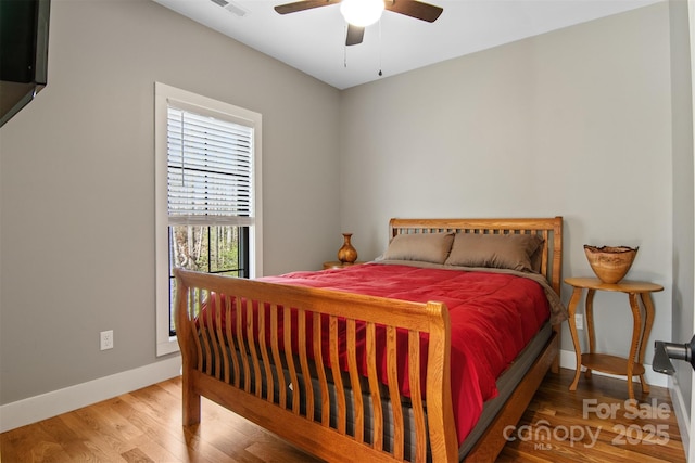 bedroom with a ceiling fan, visible vents, baseboards, and wood finished floors