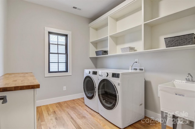 clothes washing area with washing machine and dryer, laundry area, a sink, baseboards, and light wood-type flooring