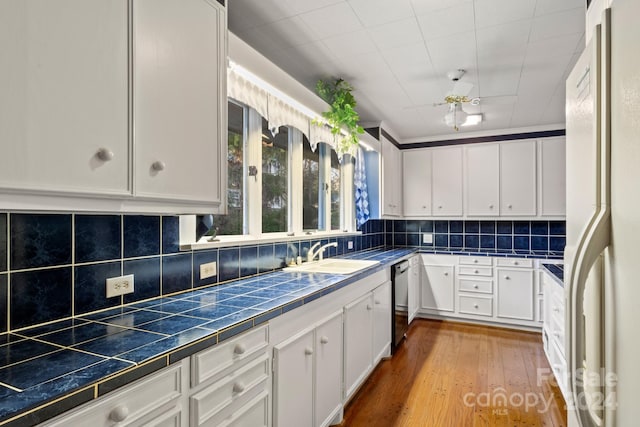 kitchen with white cabinetry, sink, tile countertops, white fridge, and light hardwood / wood-style floors