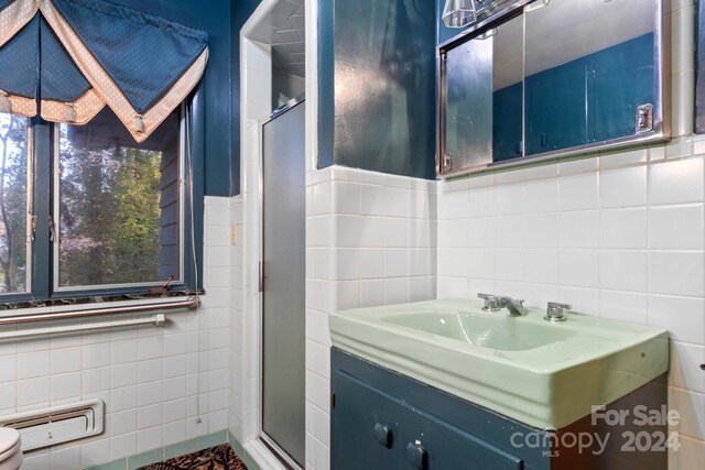 bathroom with vanity, toilet, tile walls, and a shower with shower door