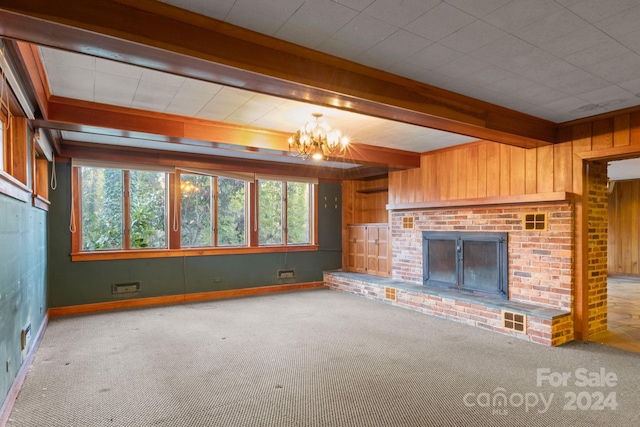 unfurnished living room featuring a fireplace, beamed ceiling, carpet floors, and an inviting chandelier