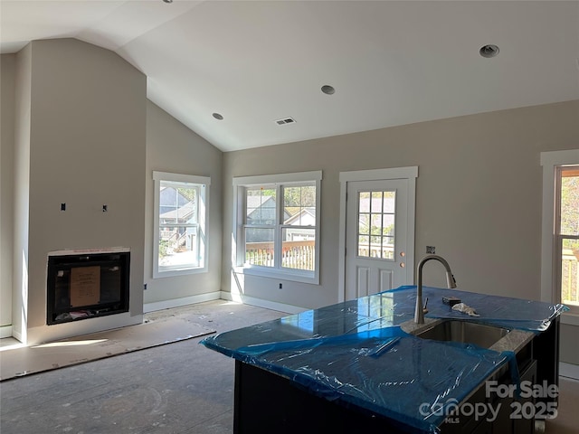 kitchen featuring vaulted ceiling, an island with sink, sink, and dark stone countertops