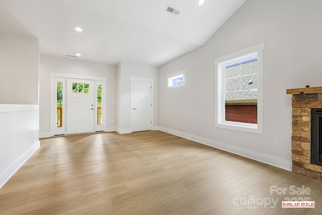 foyer entrance featuring a stone fireplace, plenty of natural light, lofted ceiling, and light hardwood / wood-style flooring