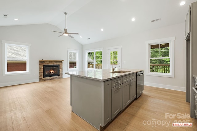 kitchen with gray cabinets, an island with sink, sink, light stone counters, and light hardwood / wood-style floors