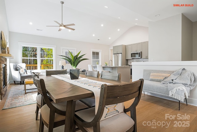 dining area featuring high vaulted ceiling, a stone fireplace, visible vents, and light wood-style floors