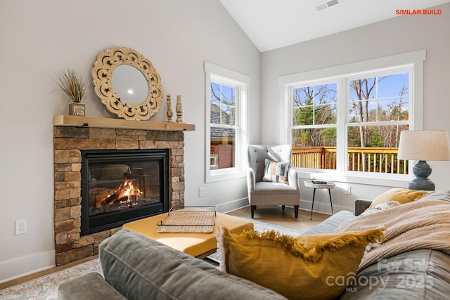 living area featuring baseboards, visible vents, wood finished floors, vaulted ceiling, and a stone fireplace