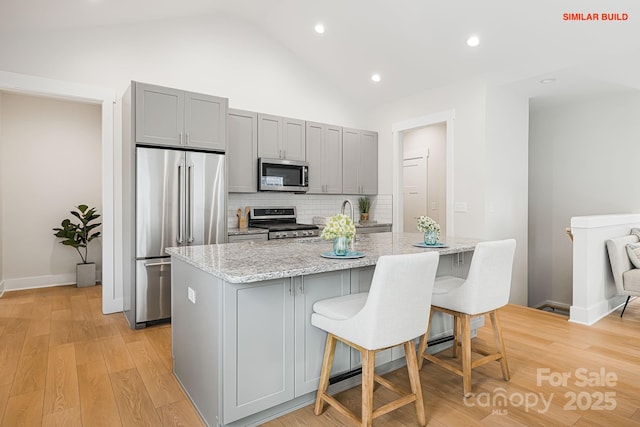 kitchen with stainless steel appliances, a breakfast bar, gray cabinets, and light stone countertops