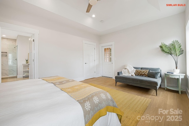 bedroom with light wood finished floors, ceiling fan, ensuite bathroom, a tray ceiling, and recessed lighting