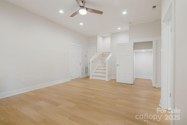 spare room featuring light wood-style floors, a ceiling fan, visible vents, and stairs