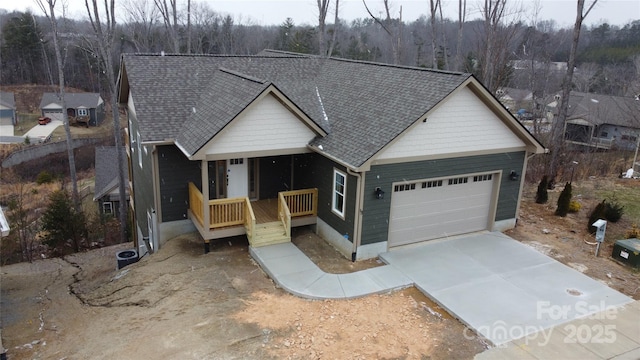 view of front of house with a shingled roof, covered porch, an attached garage, a wooded view, and driveway