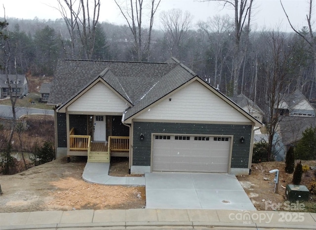 view of front facade featuring concrete driveway, a porch, an attached garage, and a view of trees