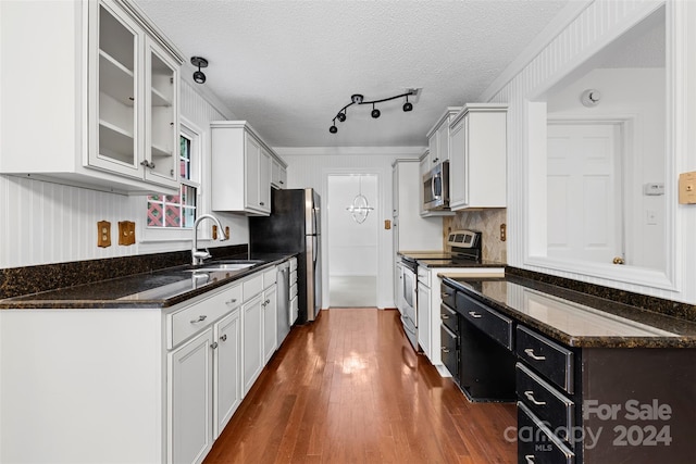 kitchen with a textured ceiling, dark wood-type flooring, white cabinetry, stainless steel appliances, and dark stone counters