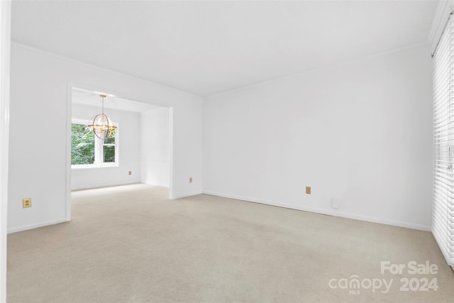 carpeted empty room featuring ornamental molding and an inviting chandelier