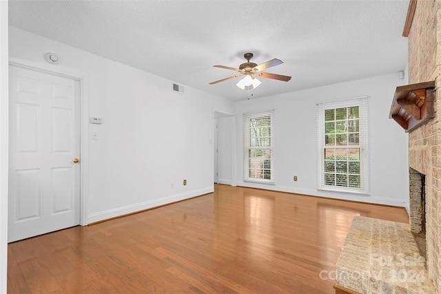 unfurnished living room featuring light hardwood / wood-style flooring, a brick fireplace, ceiling fan, and a textured ceiling