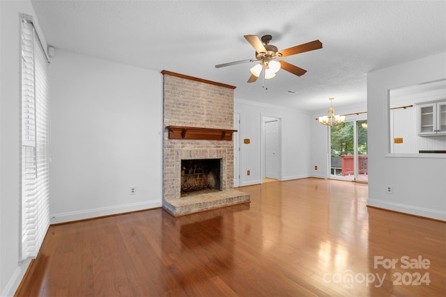 unfurnished living room featuring a textured ceiling, hardwood / wood-style flooring, ceiling fan with notable chandelier, a fireplace, and ornamental molding