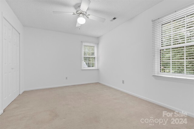 unfurnished bedroom featuring ceiling fan, a closet, light carpet, and multiple windows