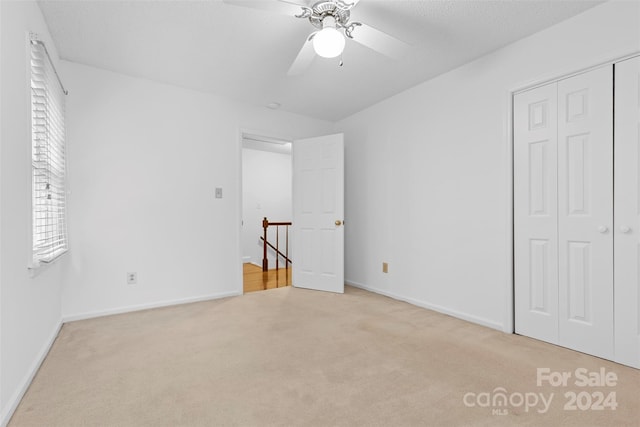 unfurnished bedroom featuring ceiling fan, light colored carpet, and a closet