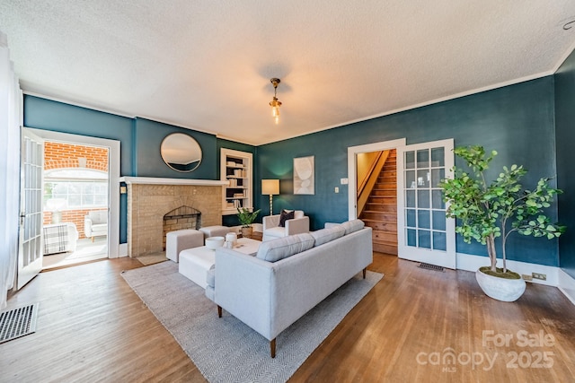 living room featuring wood-type flooring, a textured ceiling, and a brick fireplace