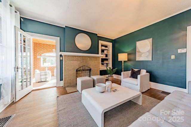 living room featuring built in shelves, hardwood / wood-style floors, a textured ceiling, and a brick fireplace