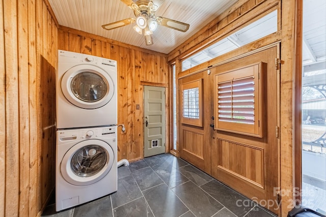 clothes washing area featuring wooden walls, ceiling fan, and stacked washer / drying machine