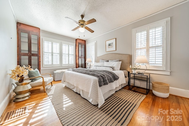 bedroom featuring ceiling fan, wood-type flooring, a textured ceiling, and ornamental molding