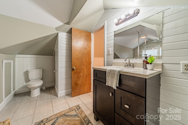 bathroom featuring wooden walls, vanity, lofted ceiling, and toilet