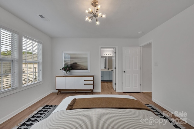 bedroom with ensuite bathroom, light wood-type flooring, and an inviting chandelier