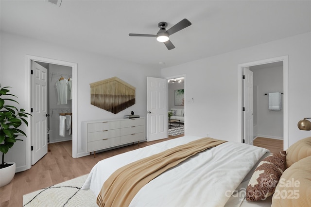 bedroom with ensuite bathroom, light hardwood / wood-style flooring, ceiling fan, and a spacious closet