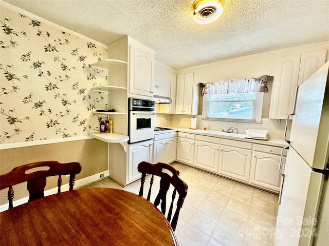 kitchen with a textured ceiling, white appliances, exhaust hood, and white cabinets