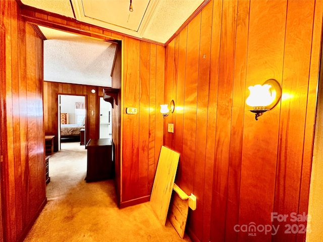 hall with light carpet, a textured ceiling, and wood walls