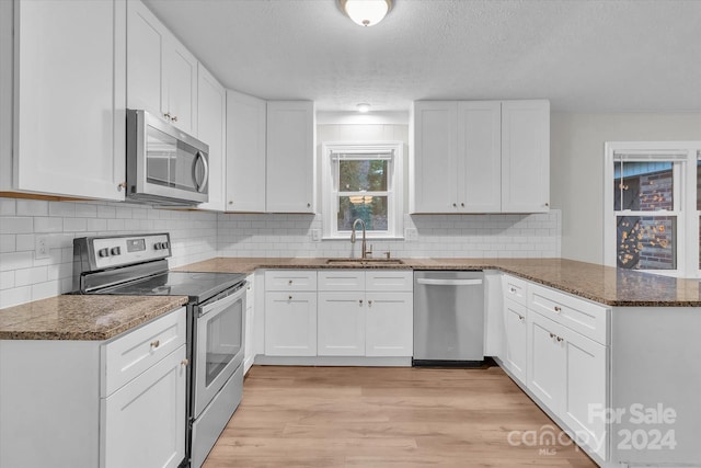 kitchen with dark stone counters, light hardwood / wood-style floors, sink, white cabinets, and appliances with stainless steel finishes