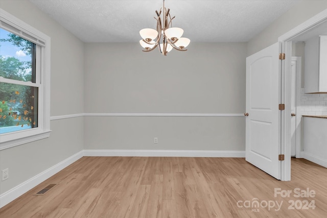 spare room featuring a textured ceiling, light hardwood / wood-style floors, and a notable chandelier