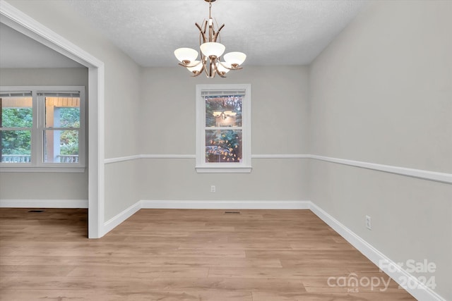 unfurnished room with light wood-type flooring, a textured ceiling, and a chandelier