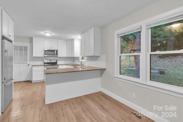 kitchen featuring sink, white cabinets, kitchen peninsula, stainless steel appliances, and dark stone countertops