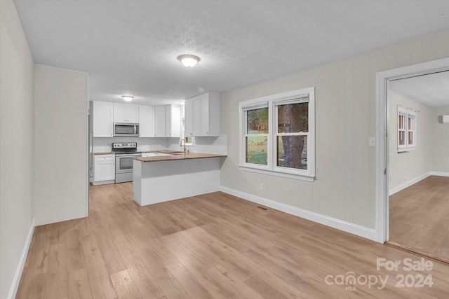 kitchen featuring white cabinets, kitchen peninsula, stainless steel appliances, light wood-type flooring, and sink