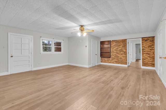 unfurnished living room with light hardwood / wood-style floors, ceiling fan, and brick wall