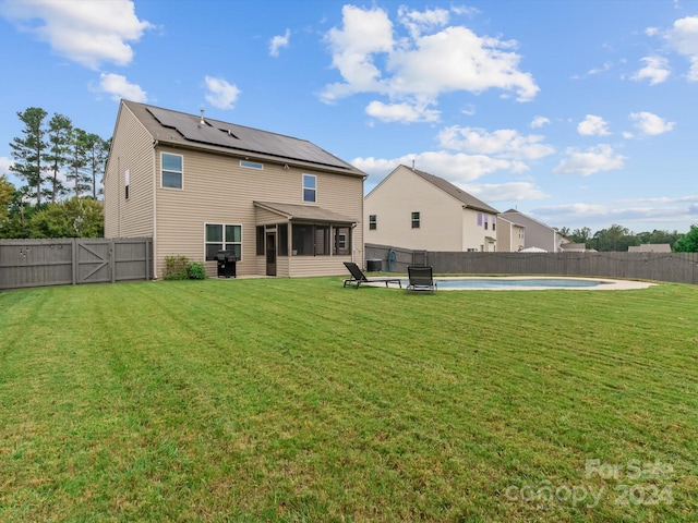 back of house featuring a lawn, a sunroom, and an empty pool