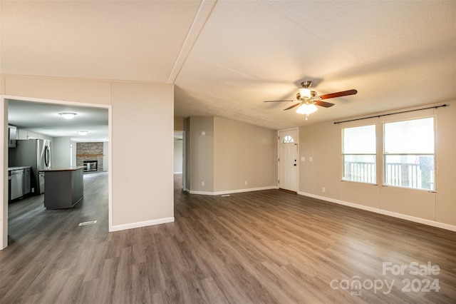 spare room featuring a textured ceiling, a fireplace, dark hardwood / wood-style flooring, and ceiling fan