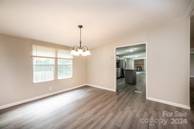 unfurnished dining area with lofted ceiling, a fireplace, dark hardwood / wood-style floors, and a chandelier