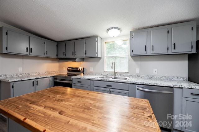 kitchen with a textured ceiling, sink, gray cabinetry, stainless steel appliances, and wooden counters