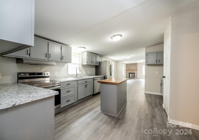 kitchen with light hardwood / wood-style floors, sink, gray cabinetry, a brick fireplace, and stainless steel appliances