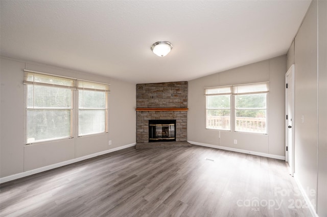 unfurnished living room featuring a textured ceiling, hardwood / wood-style floors, a stone fireplace, and lofted ceiling