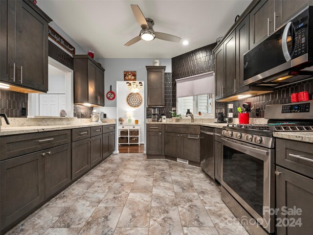 kitchen featuring decorative backsplash, light stone counters, stainless steel appliances, ceiling fan, and dark brown cabinetry