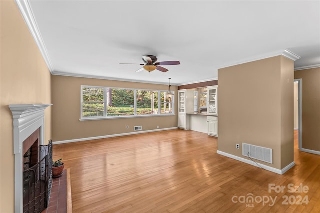 unfurnished living room with crown molding, ceiling fan, light hardwood / wood-style floors, and a brick fireplace