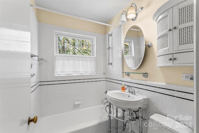 bathroom with tiled shower / bath combo, toilet, and tile walls