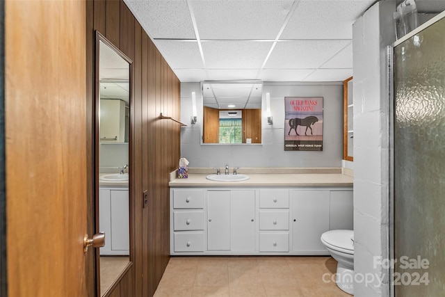 bathroom featuring a drop ceiling, vanity, a shower with door, toilet, and wood walls