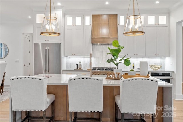 kitchen featuring white cabinetry, appliances with stainless steel finishes, a kitchen island with sink, and custom range hood