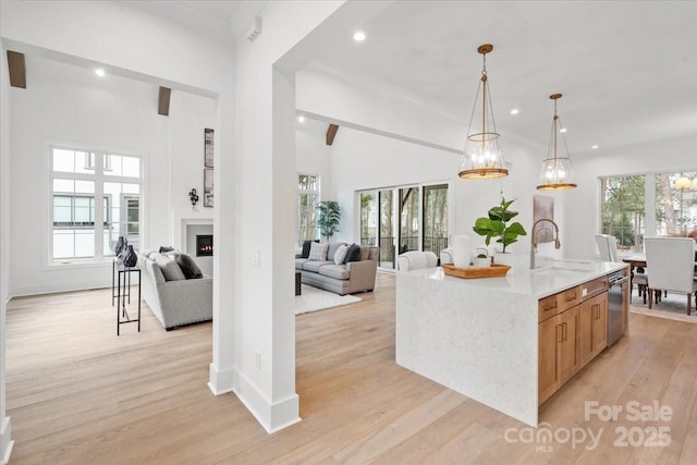 kitchen featuring decorative light fixtures, sink, stainless steel dishwasher, a center island with sink, and light wood-type flooring